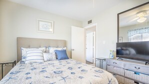 A bedroom with a bed, a television, a dresser, and a door leading to another room. - Island getaway 3 minutes from sandy beaches. (Treasure Island)