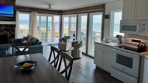 Une cuisine moderne avec vue sur l’océan, un coin repas avec une table et des chaises, et un espace salon confortable avec un téléviseur.