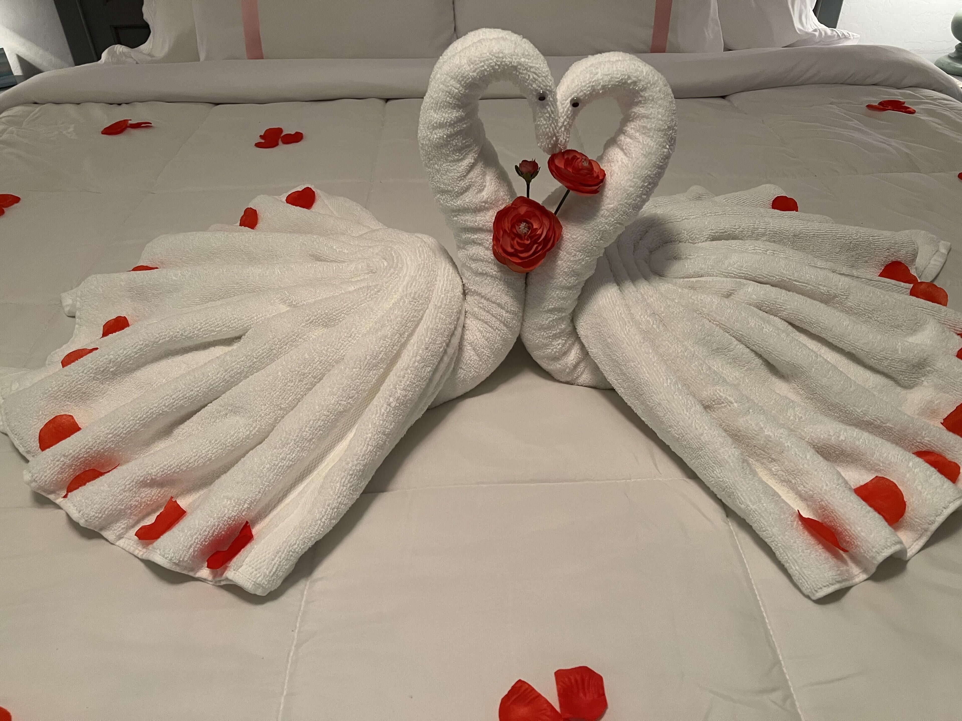 A bed with a towel arrangement in the shape of a swan, featuring red roses and red flower petals.