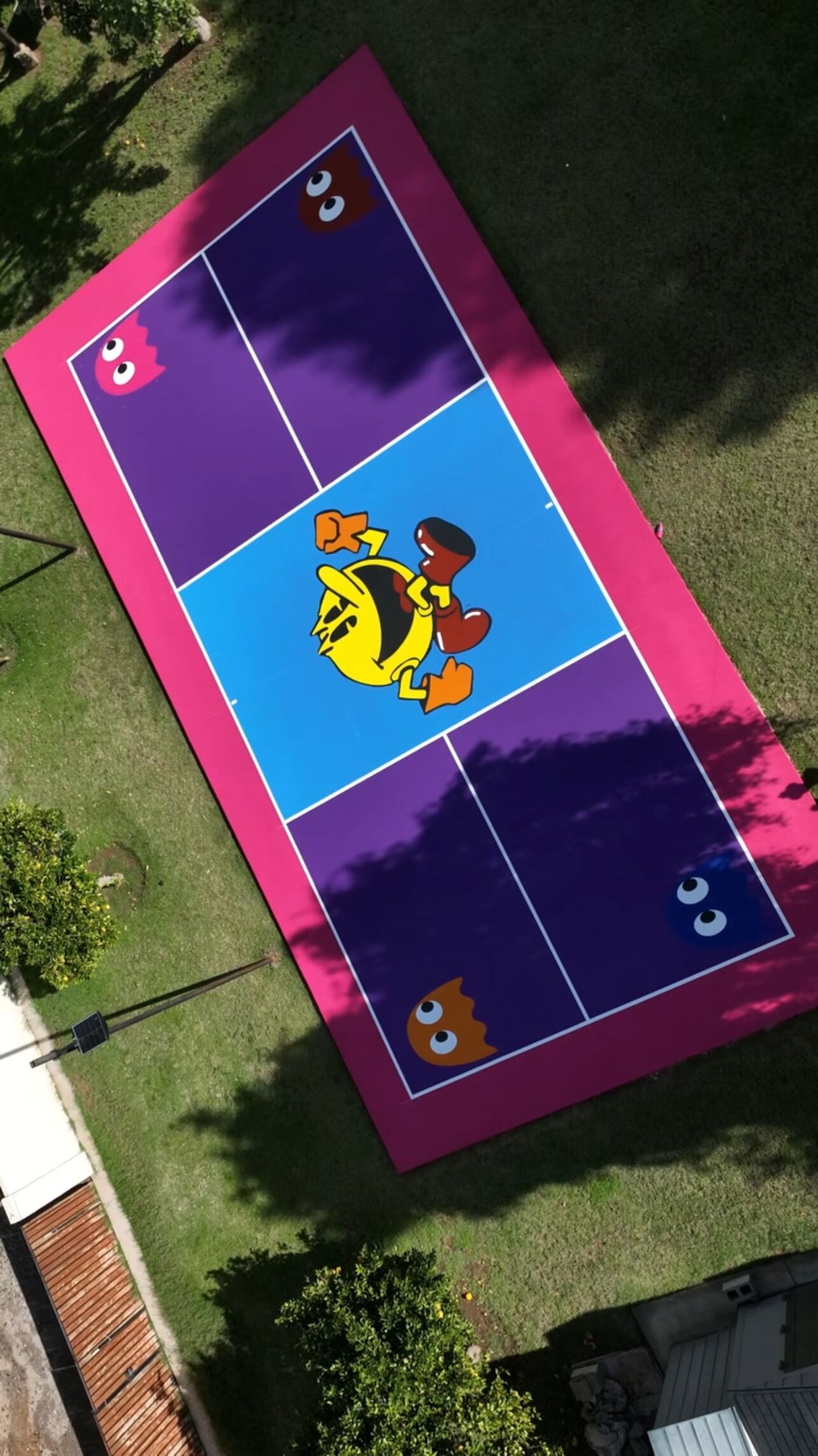 A colorful outdoor game area with a cartoon character in the center, surrounded by a purple and blue playing field with pink borders.
