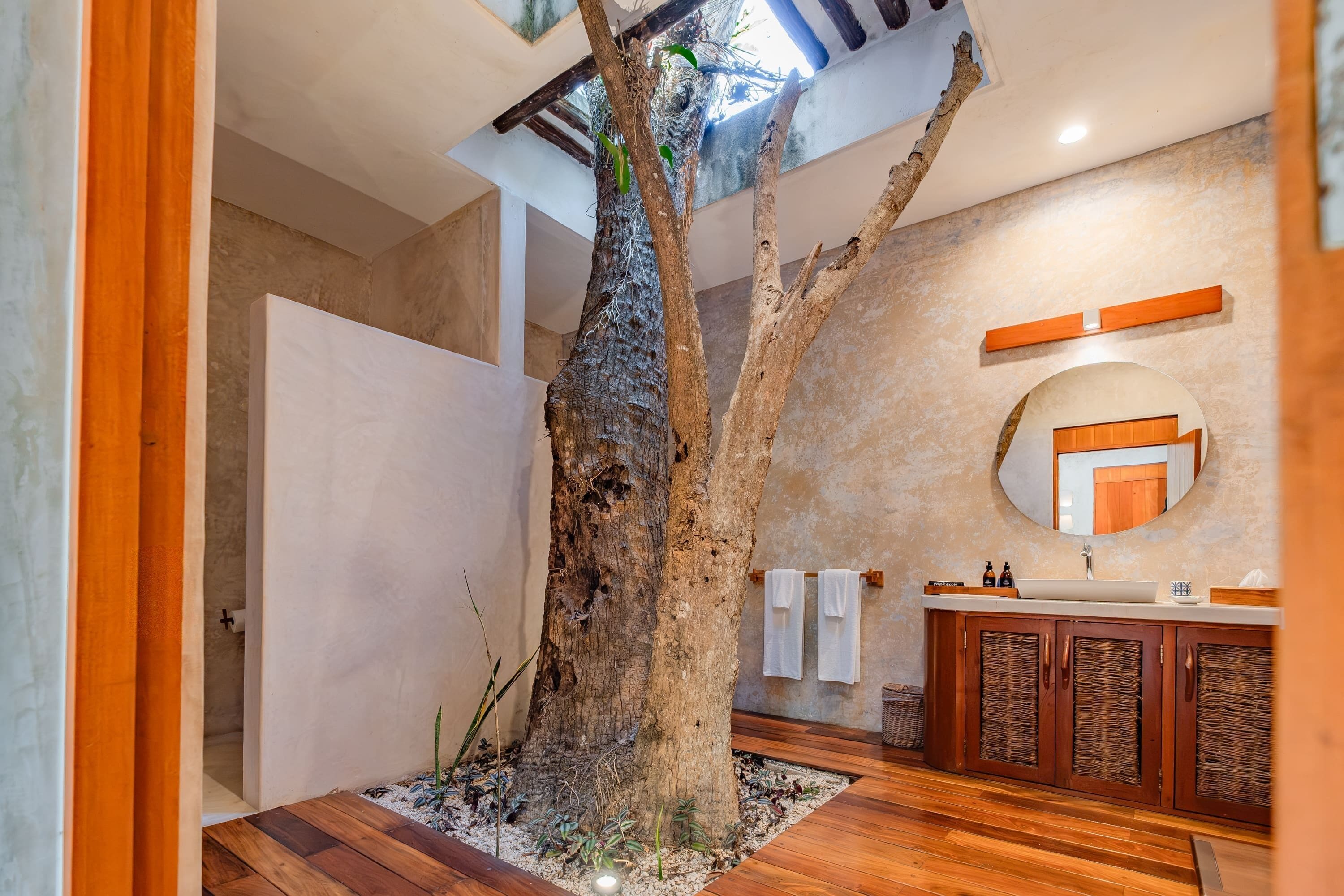 Un baño con un centro de mesa con motivos de árbol, suelo de madera, un lavabo con artículos de aseo y un espejo.