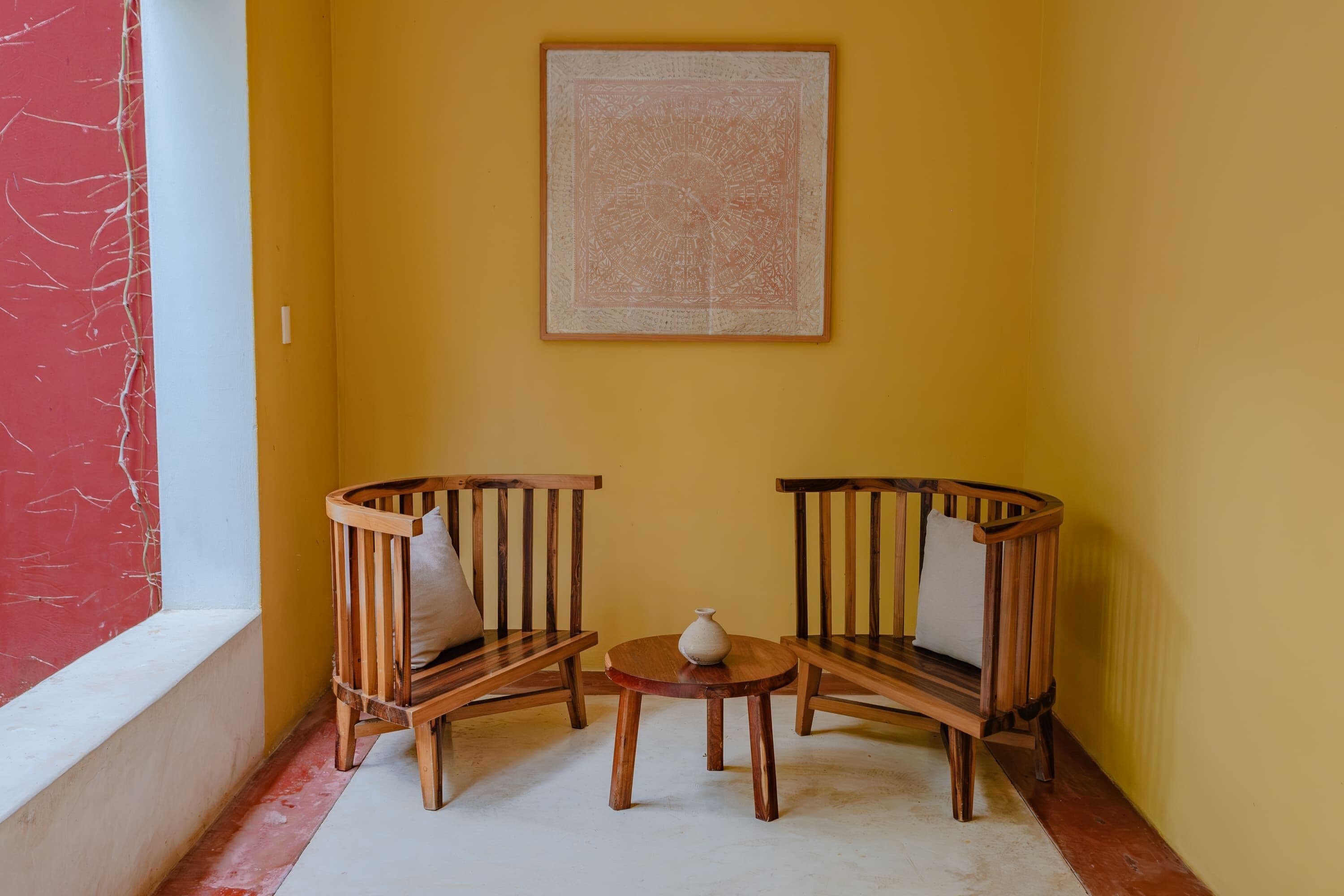 A corner room with two wooden chairs, a small table, and a vase.