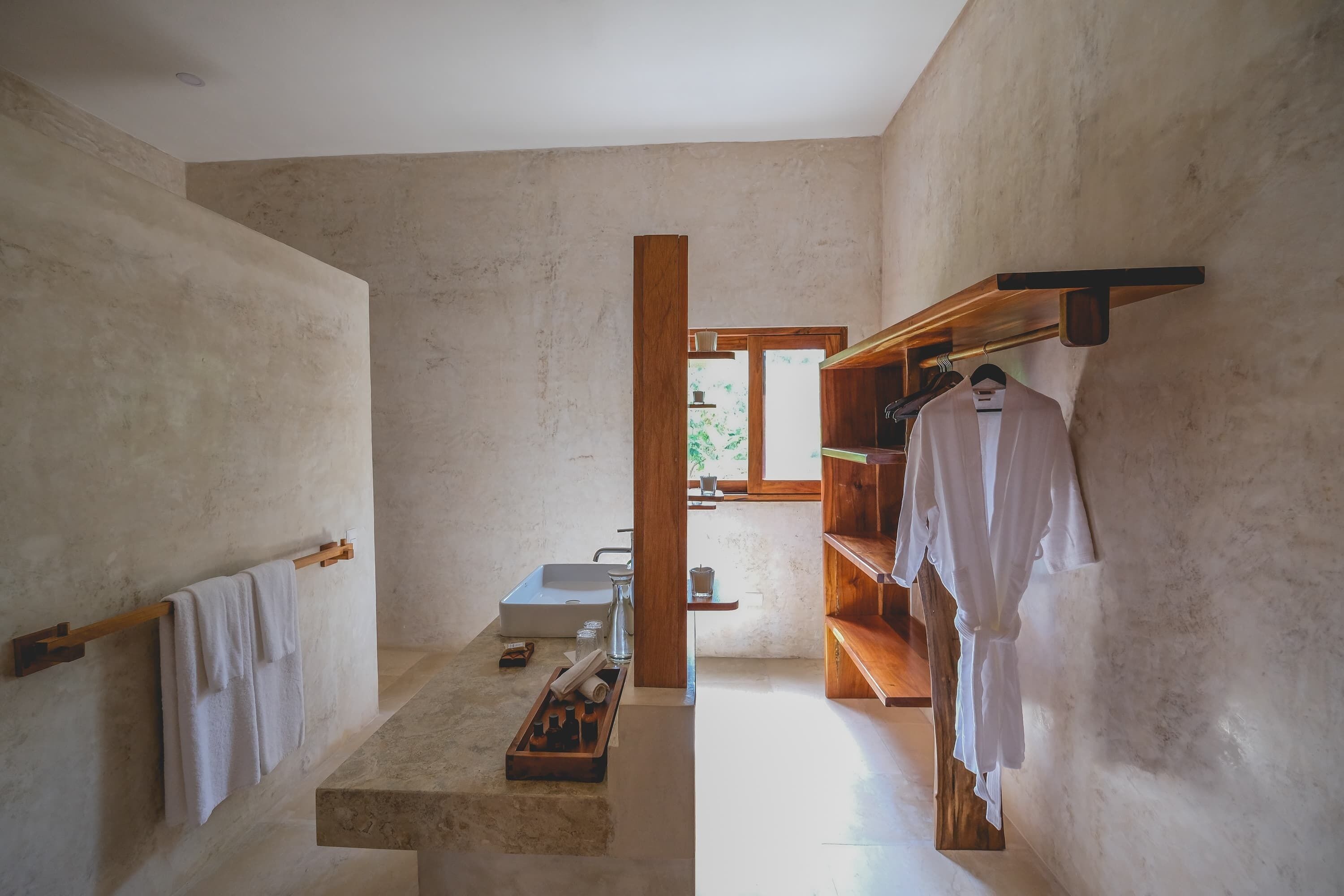 Un baño minimalista con un espejo grande, un estante de madera con toallas y un lavabo pequeño.
