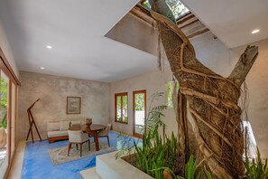 A spacious room with a large tree trunk centerpiece, a dining area with a table and chairs, and a sofa. - Wakax Hacienda - Cenote & Boutique Hotel - Small Luxury Hotels of the World (Tulum)