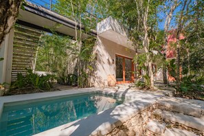 A pool area with a stone edge, surrounded by greenery and a building with a sloped roof. - Wakax Hacienda - Cenote & Boutique Hotel - Small Luxury Hotels of the World (Tulum)