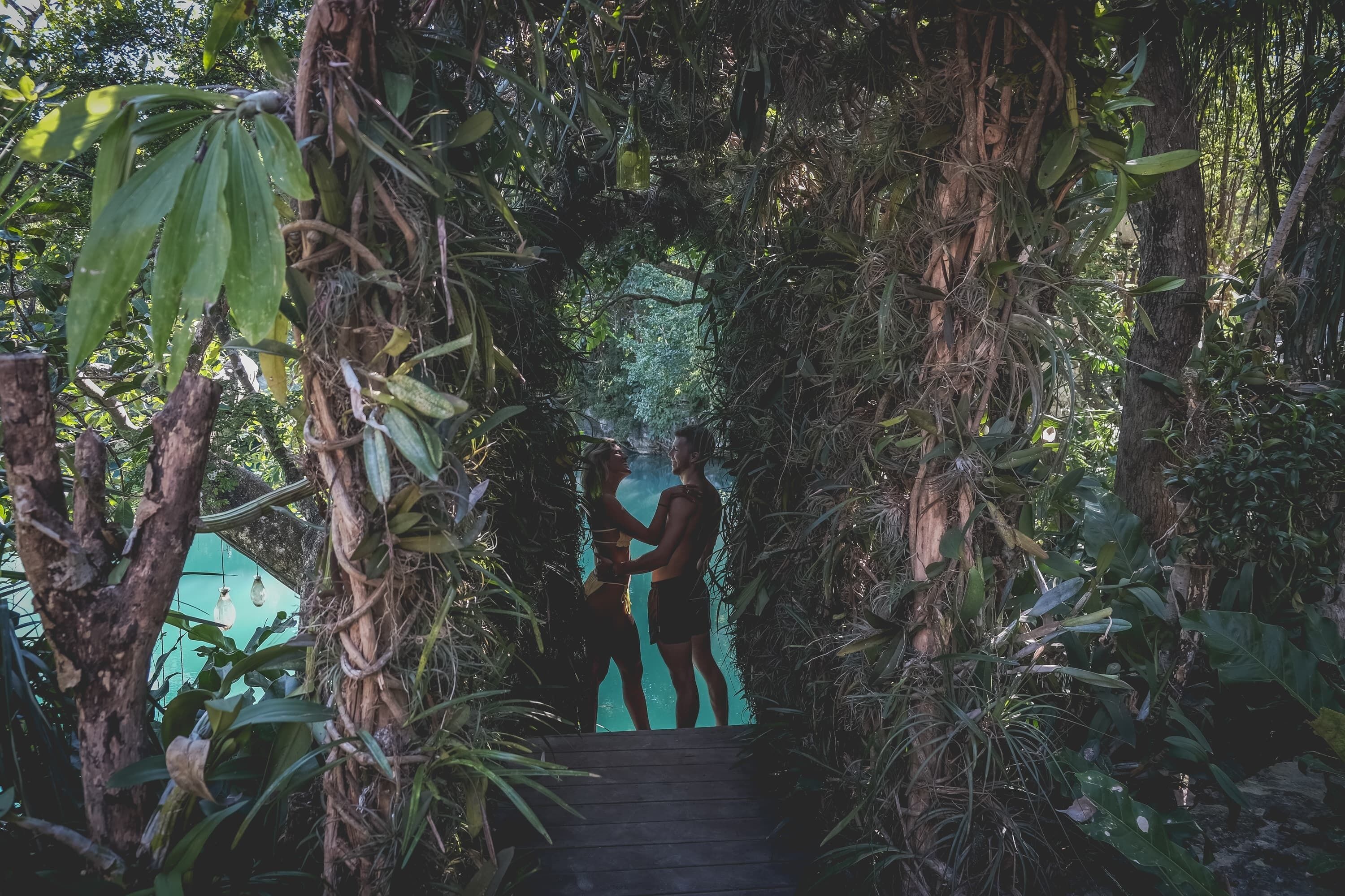 A wooden pathway surrounded by dense tropical foliage leading to a structure.