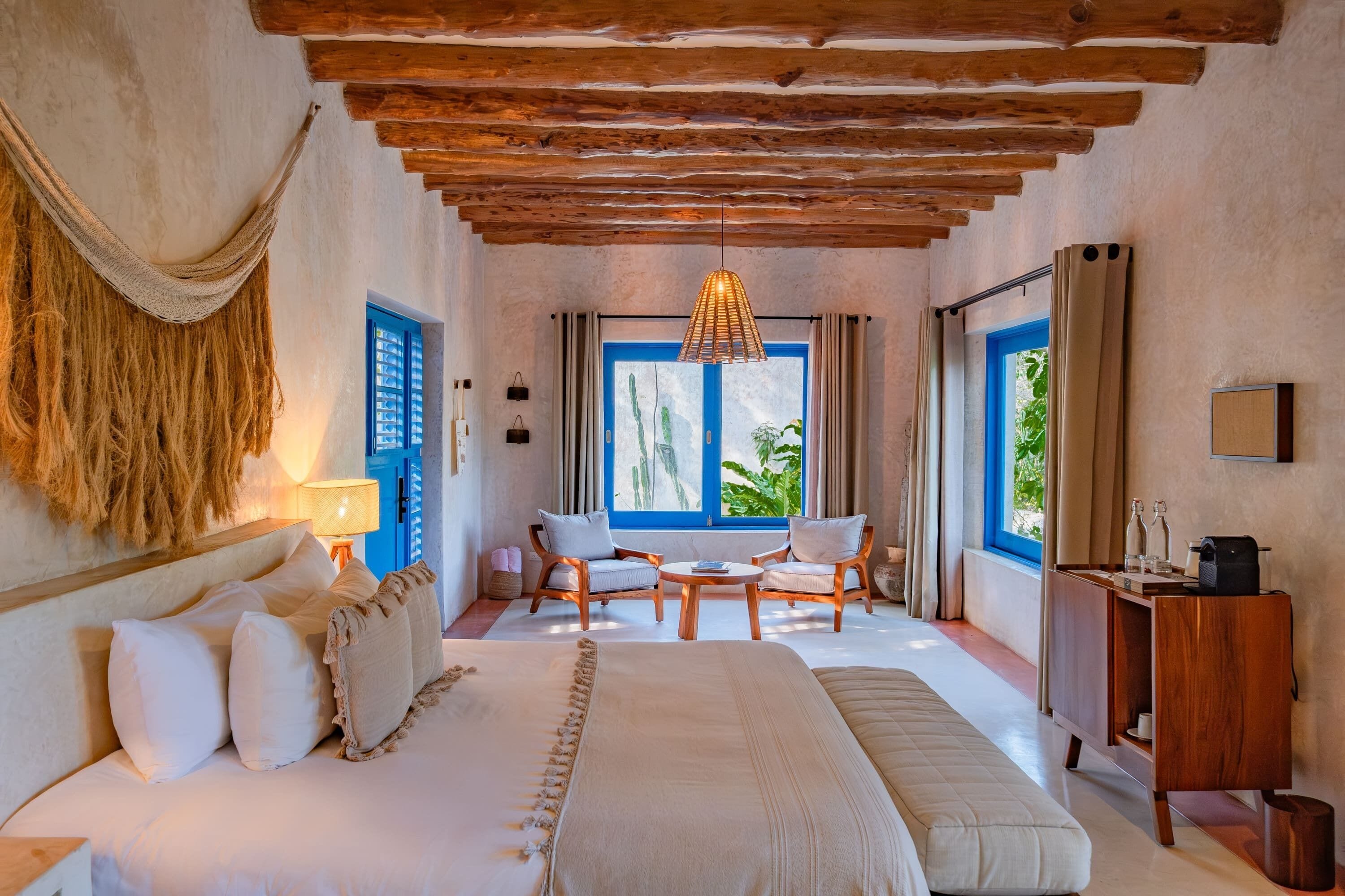 Un dormitorio amplio con una cama grande, dos sillas, un escritorio de madera y una ventana con contraventanas azules.