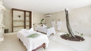 A spa room with two massage tables, a stone wall, a wooden shelf, an air conditioning unit, and a tree sculpture. - Wakax Hacienda - Cenote & Boutique Hotel - Small Luxury Hotels of the World (Tulum)