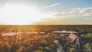 A large estate with multiple buildings surrounded by dense forest, featuring a prominent red barn and a white house with a large porch. - Wakax Hacienda - Cenote & Boutique Hotel - Small Luxury Hotels of the World (Tulum)