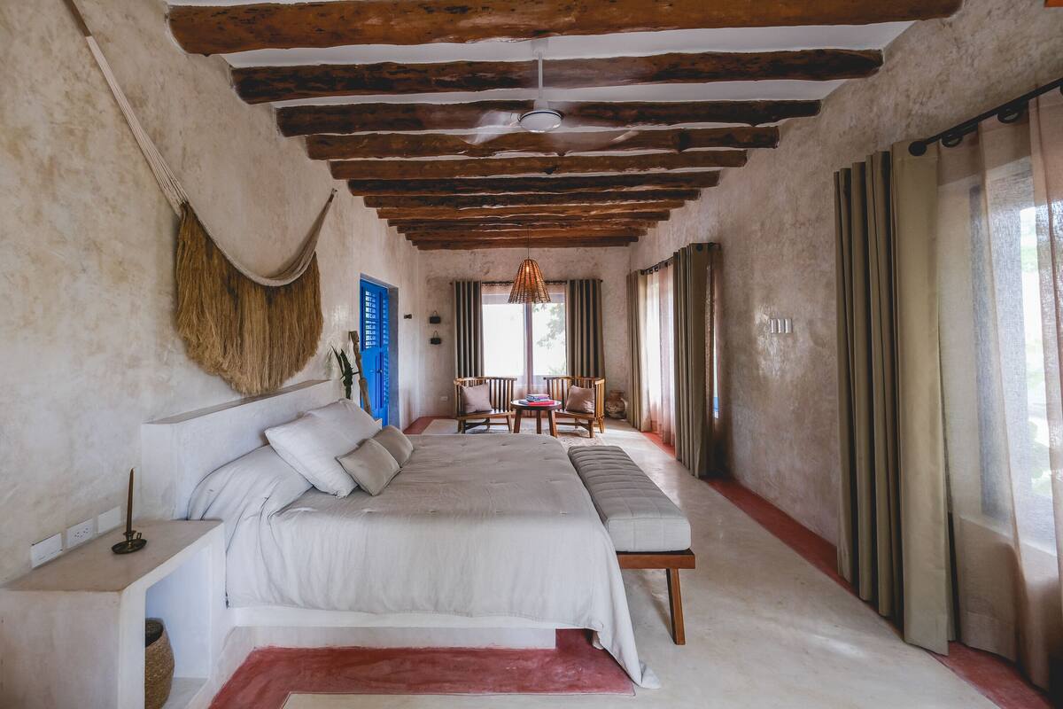 A bedroom with a large bed, a bedside table, a bench, and a small table with chairs.