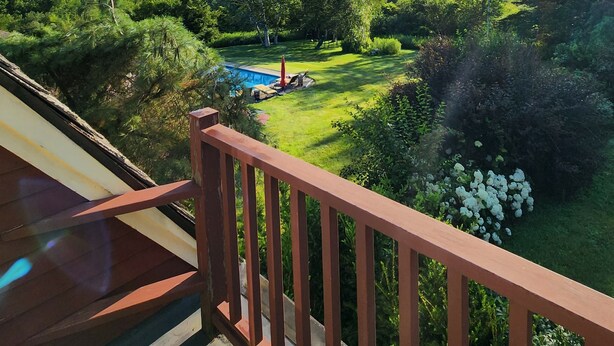 A balcony with a view of a well-maintained garden, a swimming pool, and distant mountains. - A cozy home nestled in the Green Mountains of Vermont! (Pownal)