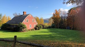A red house with a sloped roof, surrounded by a well-maintained lawn and a wooden fence. - A cozy home nestled in the Green Mountains of Vermont! (Pownal)