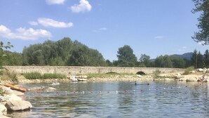 Ein klarer Fluss mit Steinen und einer Steinbrücke im Hintergrund.