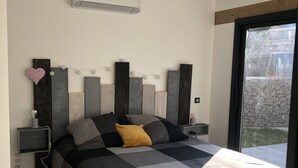 Ein modernes Schlafzimmer mit Bett, Nachttischen, einer Klimaanlage und Blick ins Freie.