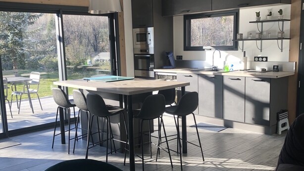 Eine moderne Küche mit eingebauten Geräten, ein Essbereich mit großem Tisch und Stühlen sowie ein Blick ins Freie.