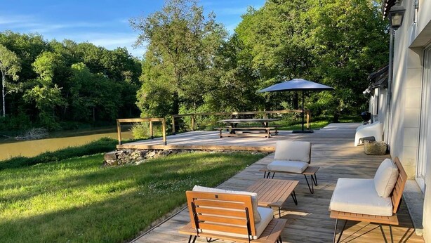 Une terrasse en bois avec des meubles d’extérieur, un belvédère et une vue sur une rivière et des arbres.