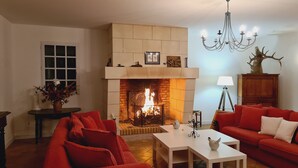 Un salon avec une cheminée, des canapés rouges, une table basse blanche et un lustre.