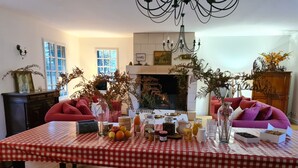 Un coin repas avec une nappe à carreaux rouges et blancs, une cheminée et deux canapés.