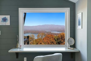 Ein Zimmer mit großem Fenster und Blick auf eine malerische Seenlandschaft im Herbst.