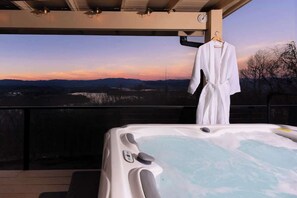 Una vasca idromassaggio su un balcone con vista su un tramonto e montagne.