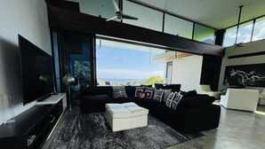 Ein modernes Wohnzimmer mit großem Fernseher, einem Ecksofa und Blick ins Freie.