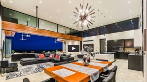 Ein modernes Wohnzimmer mit einer großen Couch, einem Essbereich mit einem zentralen Tisch und einer Küchenzeile.