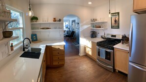 A modern kitchen with white countertops, stainless steel appliances, and wooden flooring. There is a view into the adjacent living area through an archway. - Swede Hill Suite (Moscow)