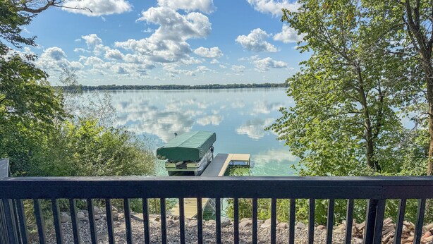 Blick auf einen See von einer Holzdielen-Terrasse mit Metallgeländer, mit ruhigem Wasser und einer entfernten Uferlinie.