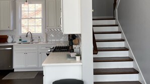Una cocina moderna con armarios blancos, una isla central y una escalera de madera que sube a un segundo piso.