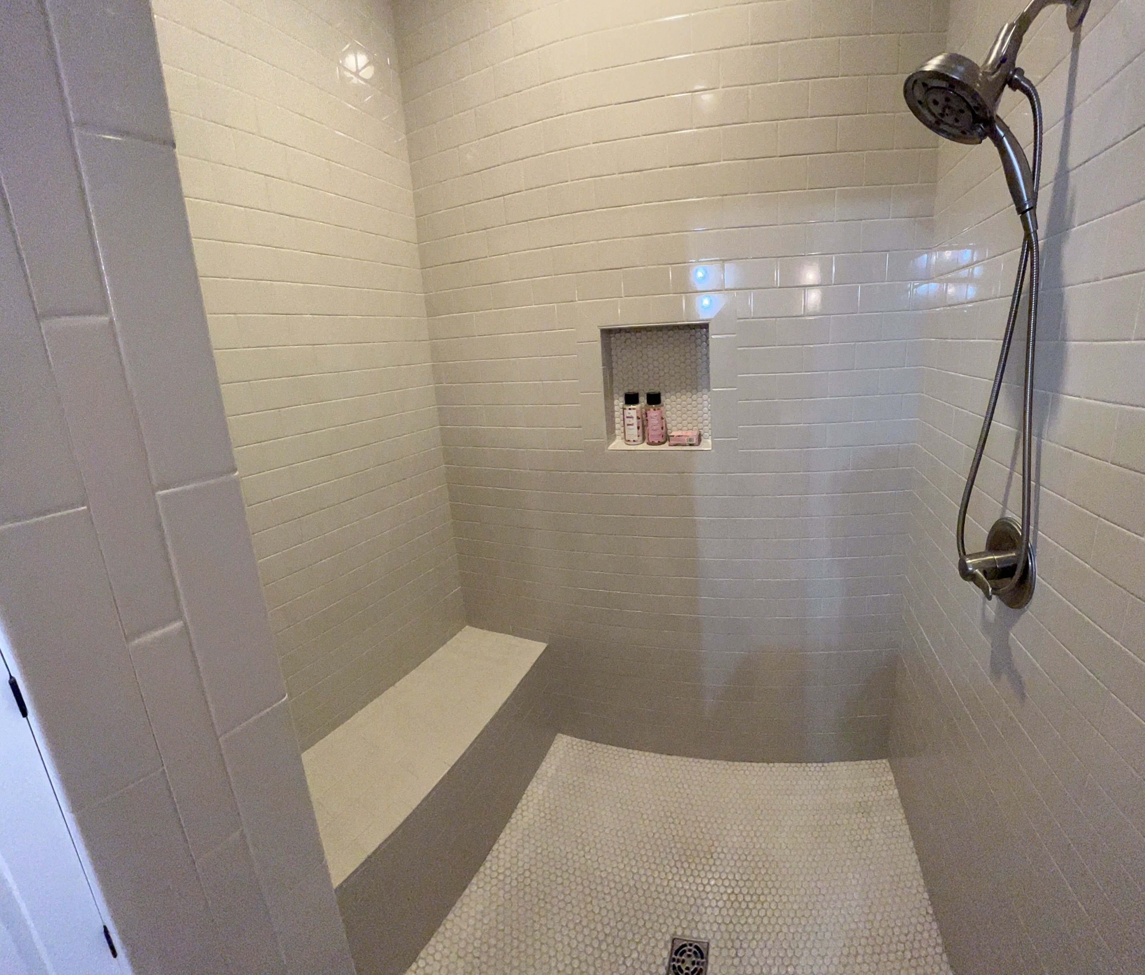 A modern shower area with a tiled wall, a handheld showerhead, and a small shelf with toiletries.