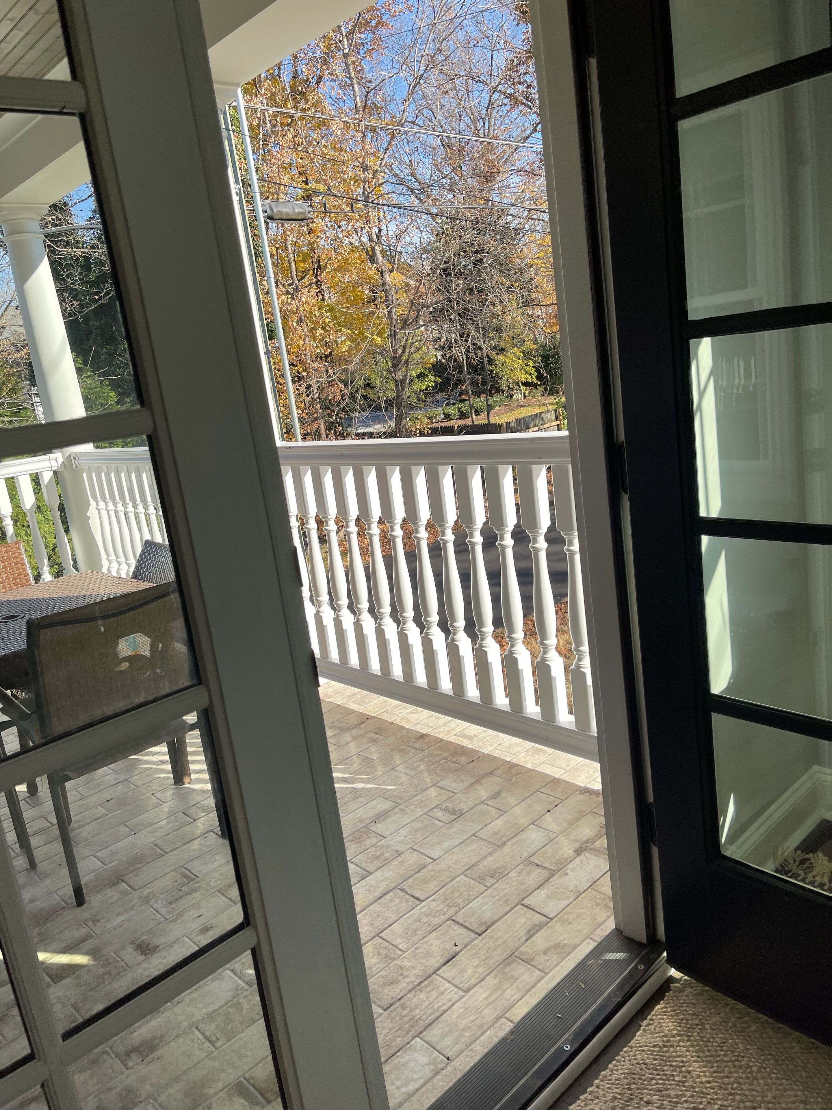 A view from inside a room to a balcony with a white railing, a tiled floor, and a chair.