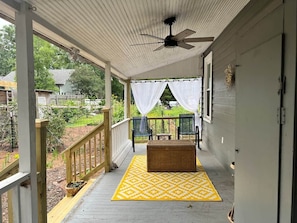 A covered porch with a ceiling fan, a yellow patterned rug, and two chairs.