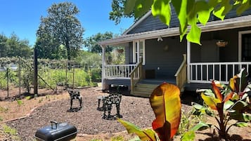A house with a porch, a barbecue grill, and a garden with plants and a metal sculpture.