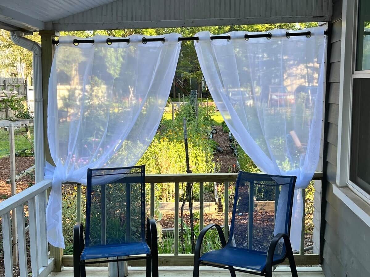 A covered porch with two chairs and white curtains.