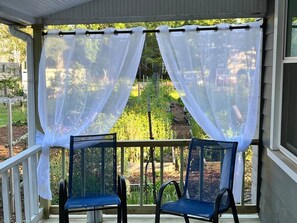 A covered porch with two chairs and white curtains.
