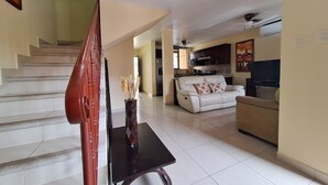 A living room with a sofa, a TV, and a staircase. - Villa in a Quiet and Safe Residential Area for 6 people. (Comunidad, Carrillo)