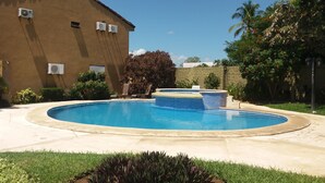 A swimming pool with a hot tub, surrounded by a garden and a building with air conditioning units. - Villa in a Quiet and Safe Residential Area for 6 people. (Comunidad, Carrillo)