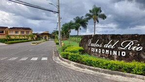 A paved road leading to a gated entrance with a stone wall and greenery. - Villa in a Quiet and Safe Residential Area for 6 people. (Comunidad, Carrillo)