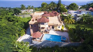 A large, multi-story house with a swimming pool, surrounded by lush greenery and palm trees. - Ocean View Terrace (Montego Bay)