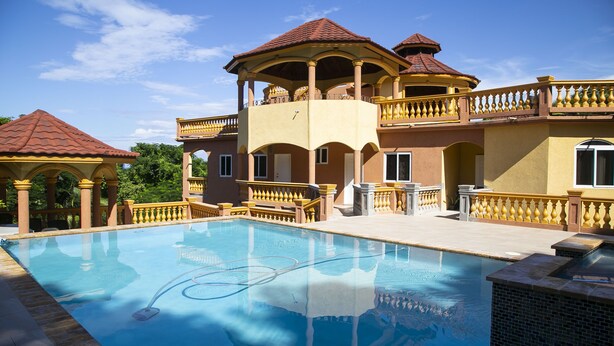 A large swimming pool with a hot tub, surrounded by a multi-level building with balconies and a red-tiled roof. - Ocean View Terrace (Montego Bay)