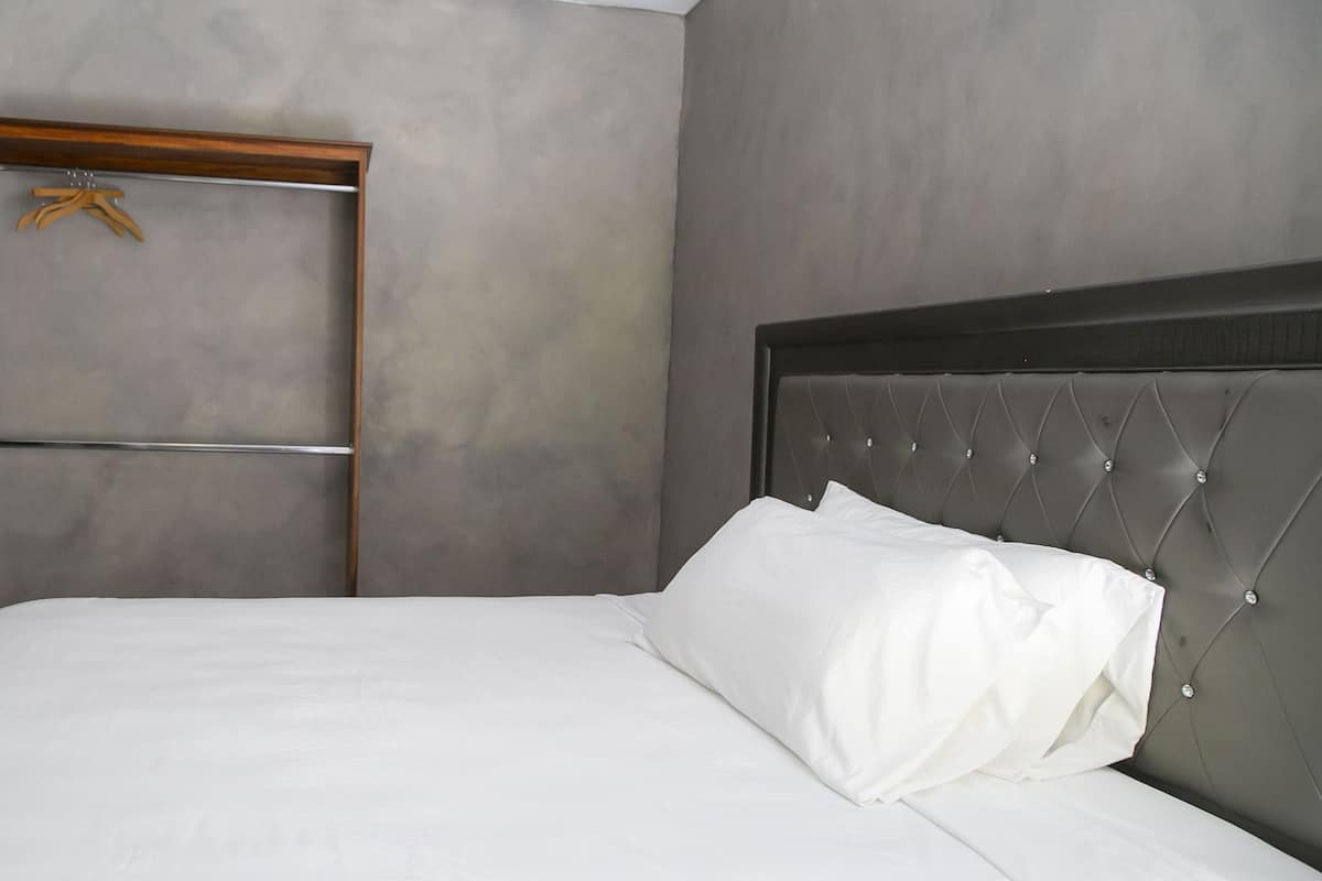 A neatly made bed with white linens in a room with a grey wall and a wooden door.