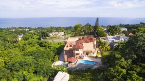 A large house with multiple red-roofed structures, a swimming pool, and lush greenery surrounding it. - Ocean View Terrace (Montego Bay)
