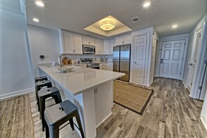 Une cuisine moderne avec des meubles blancs, un îlot central doté de tabourets, des appareils en acier inoxydable et un luminaire au plafond.