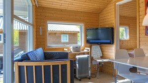 Ein gemütliches Blockhaus mit Holzvertäfelung, einem an der Wand montierten Fernseher, einer Couch, einem Tisch und einem Heizkörper.