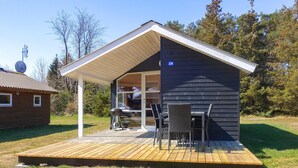 Eine kleine Hütte mit überdachter Terrasse, Grill und Essbereich.