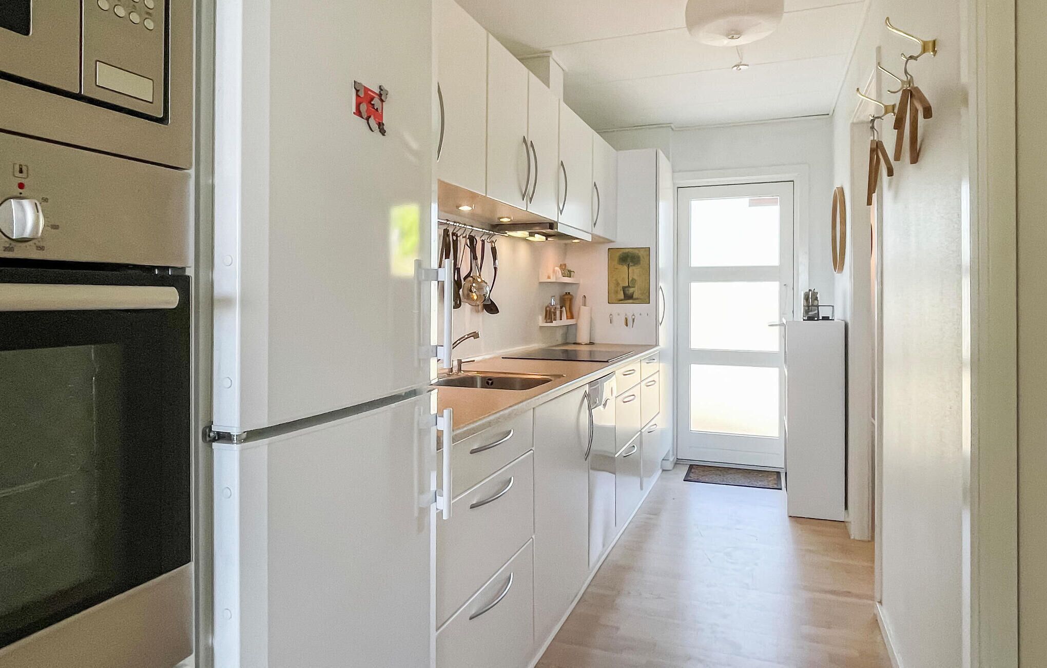 A modern kitchen with white cabinetry, a built-in oven, and a stainless steel range hood. There is a window providing natural light and a door leading to another room.