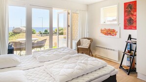 A bedroom with a large bed, a view of the beach, and a window with a view of the sea.