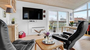 Een moderne woonkamer met een flatscreen televisie, comfortabele zithoek, een houten salontafel en grote ramen met uitzicht op het landschap.