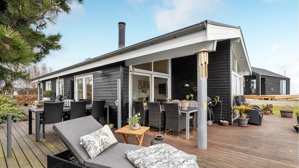 Een modern huis met een overdekte patio, compleet met buitenmeubilair, een eettafel en een zithoek.