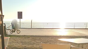 A beachside café with outdoor seating, a bicycle in the background, and a bottle on the table.